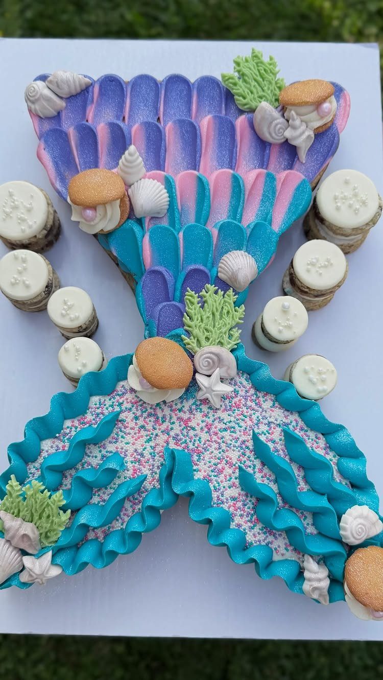 Mermaid tail cookie cake with blue frosting, seashells, and colorful sprinkles.