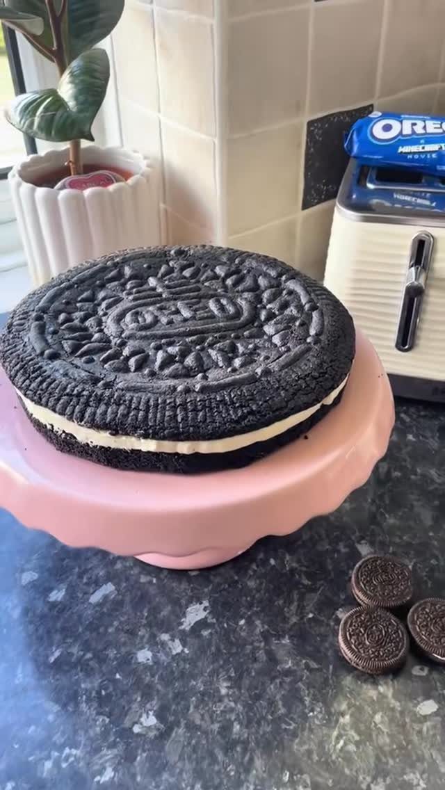 Giant Oreo cookie cake on a pink stand with real cookies nearby.