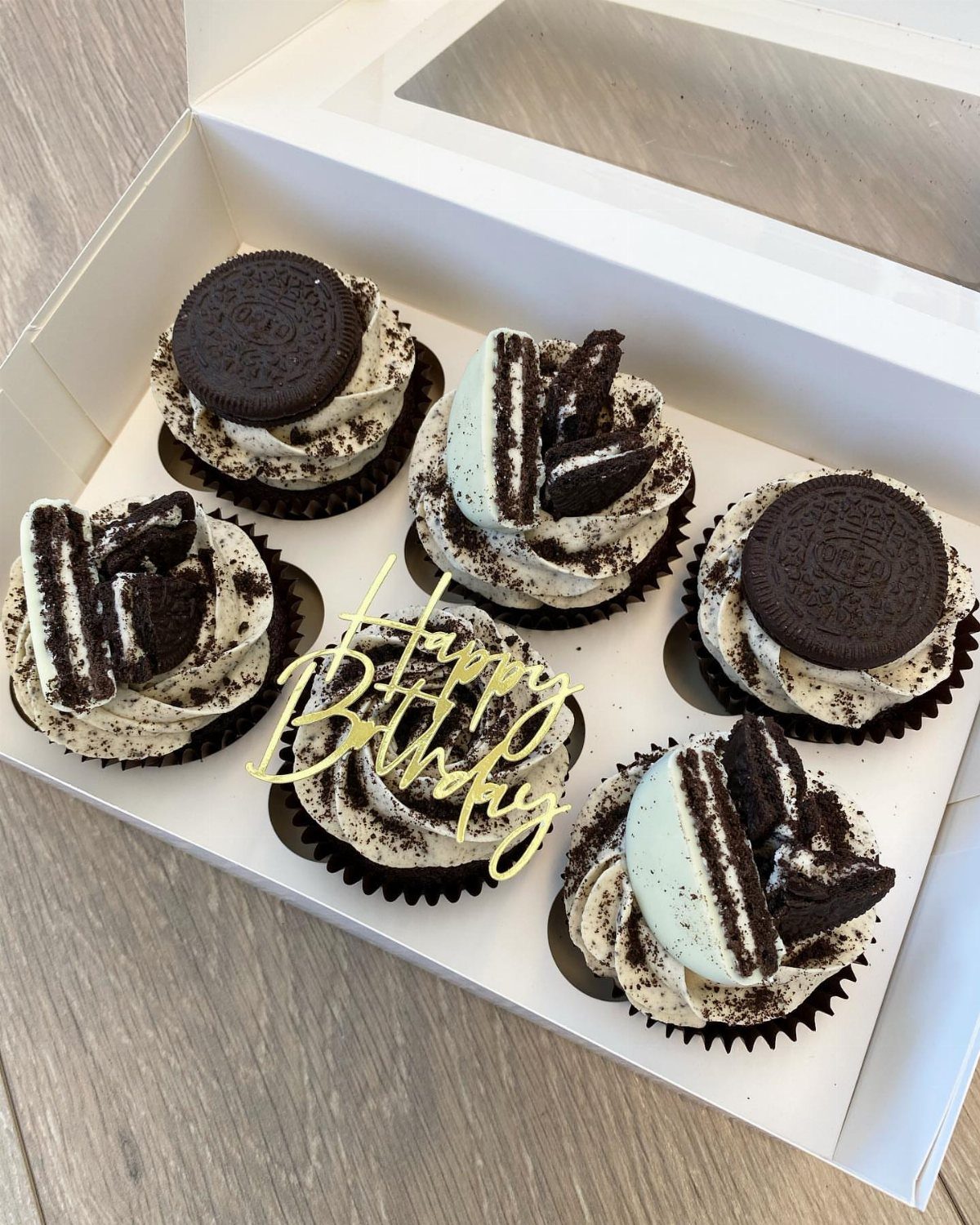 Chocolate cupcakes with white frosting and Oreo cookies in a white gift box.