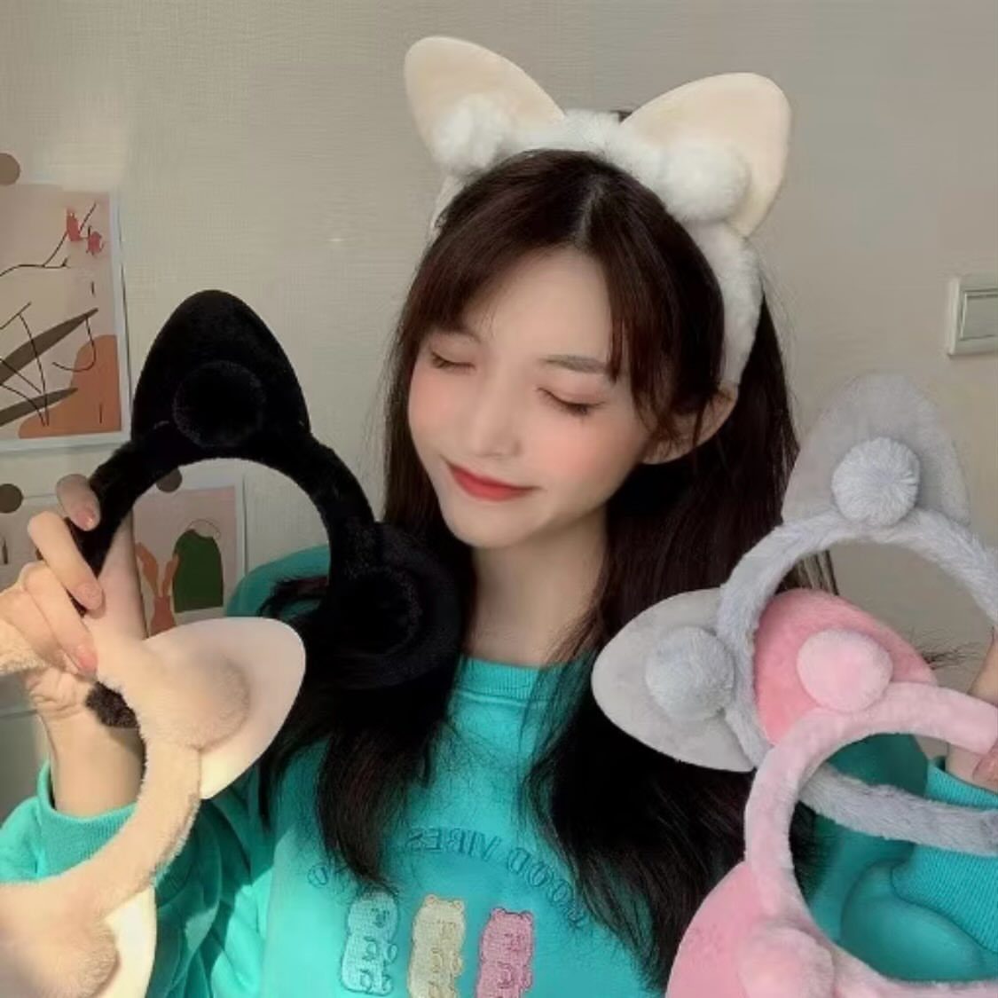Woman wearing white cat-ear headbands and holding black, grey, and pink versions.