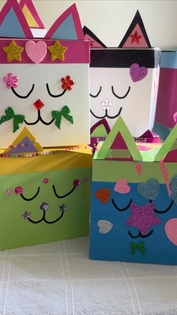 Colorful gift boxes decorated as cat faces with glittery stars and paper ears.