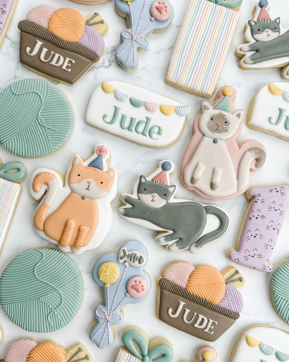 Cat shaped sugar cookies with royal icing and party themes on marble surface