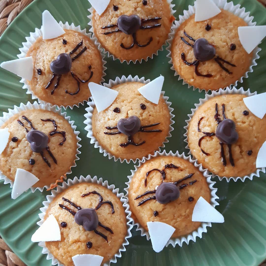 Cat-faced muffins with chocolate whiskers and white paper ears on a green plate
