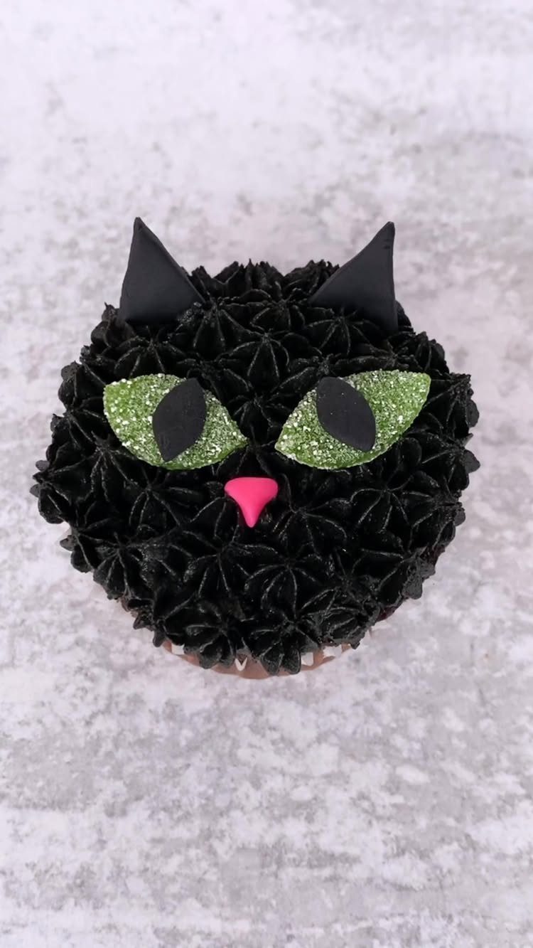 Black cupcake decorated as a cat face with green glittery eyes and pink nose.