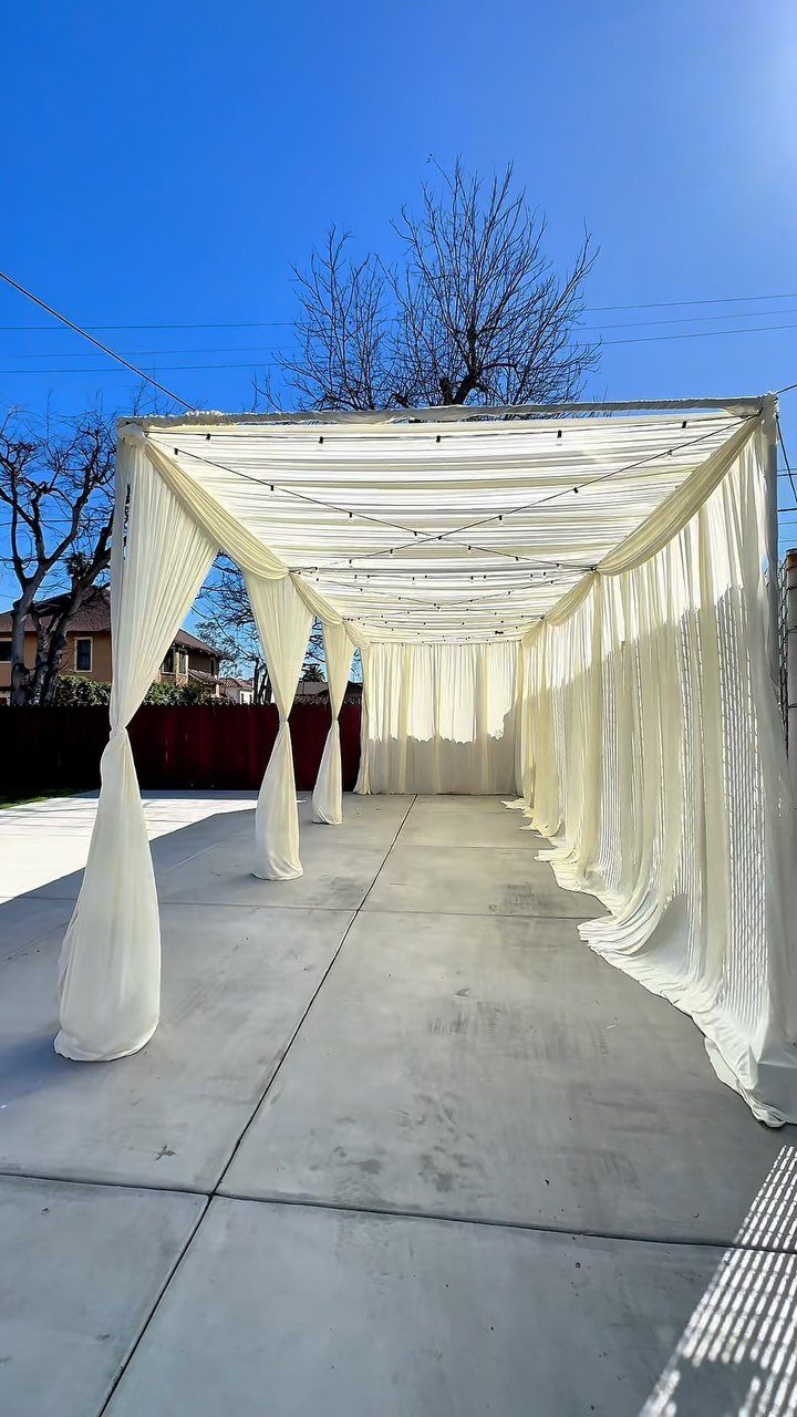 White sheer fabric draped over an outdoor arbor canopy on a concrete patio