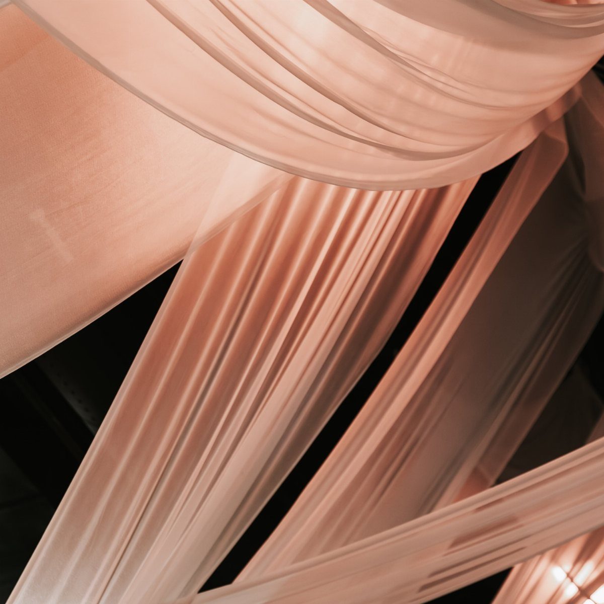 White sheer fabric drapes hanging in elegant folds from a dark ceiling.