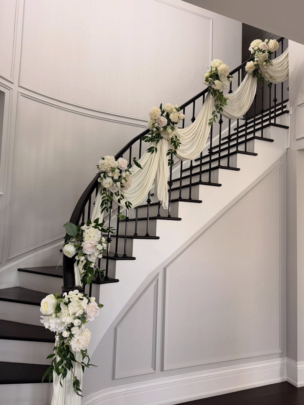 White fabric swags and floral bouquets decorating a curved black staircase railing.