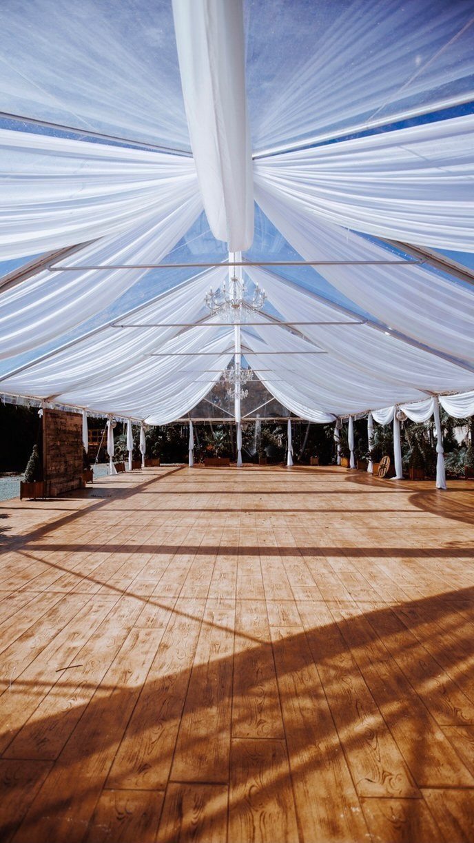 White sheer fabric draped across a clear tent ceiling over a wooden floor