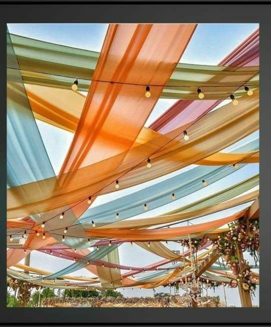 Multi-colored sheer fabric panels draped across a ceiling with hanging string lights.
