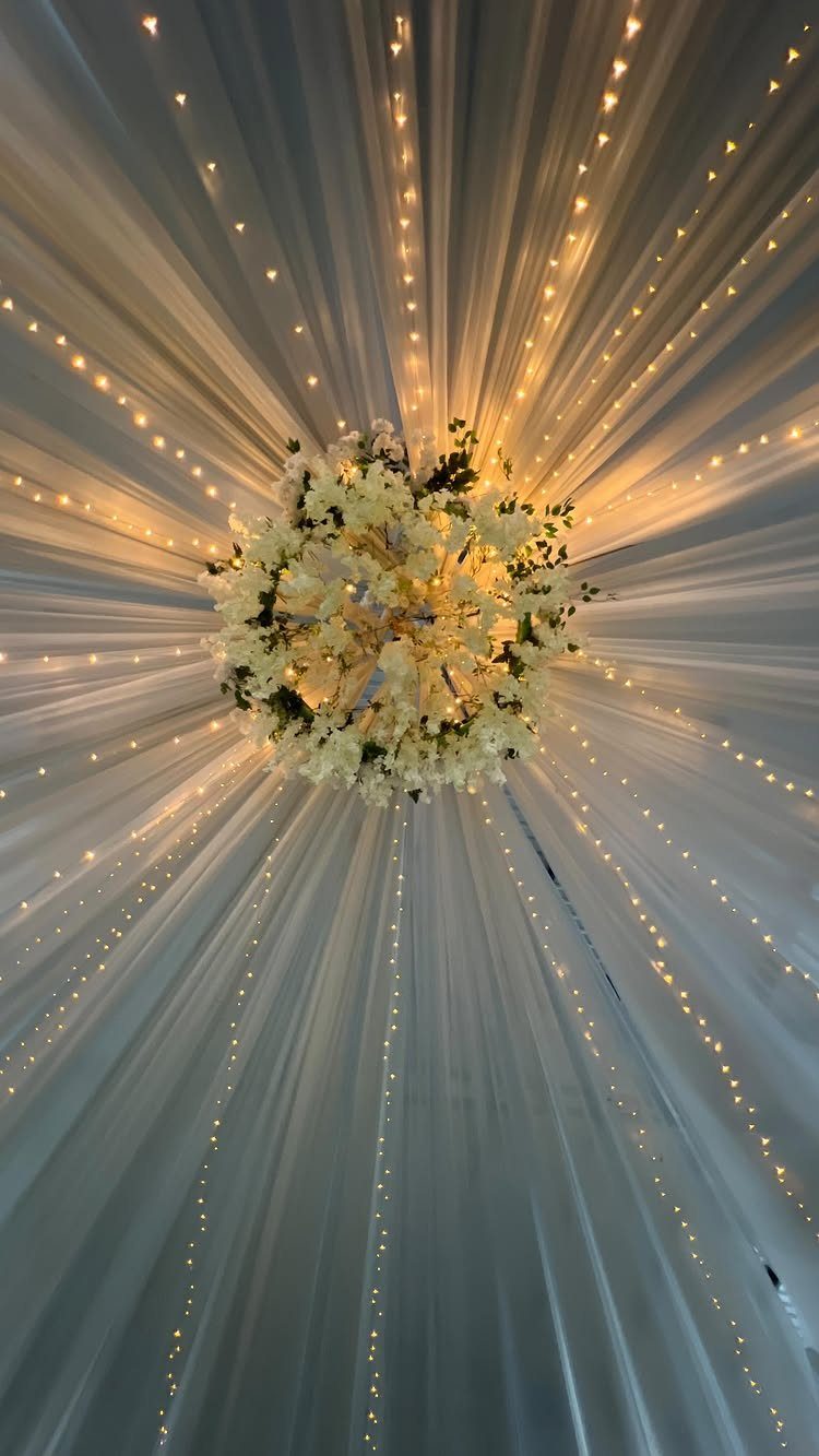 White ceiling drapes radiating from a central floral arrangement with fairy lights.