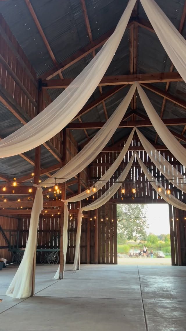 White fabric ceiling drapes and string lights inside a rustic wooden barn venue