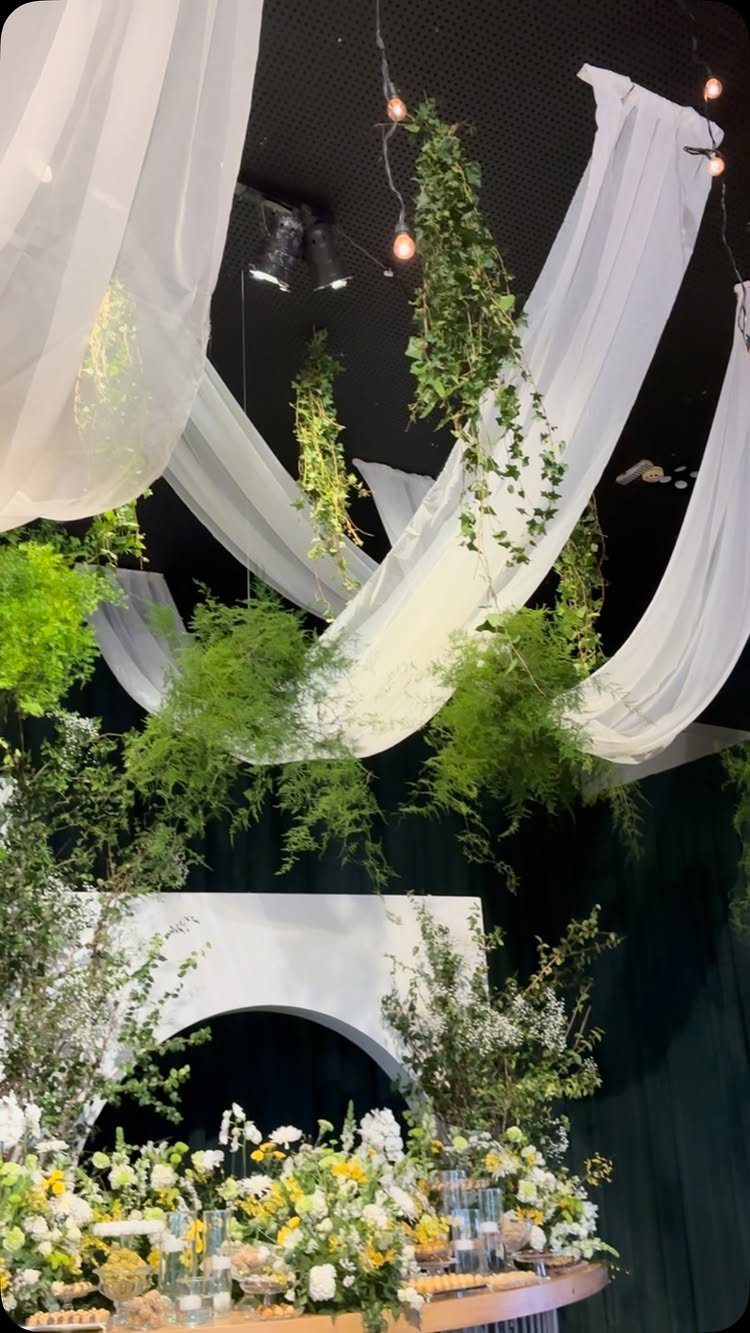 White sheer ceiling drapes interwoven with hanging greenery and warm fairy lights.