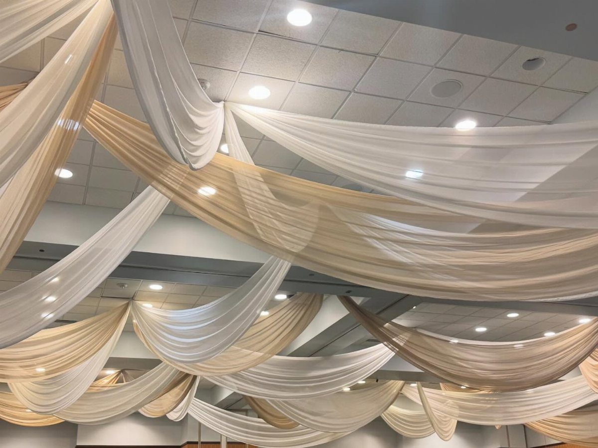 White and champagne fabric drapes swooping across a white tiled event ceiling.