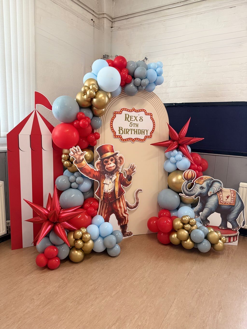 Balloon arch in red, blue, and gold framing a circus party backdrop.