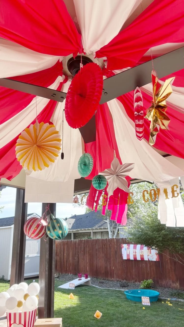 Circus party decorations with red and white fabric ceiling and colorful hanging paper ornaments.