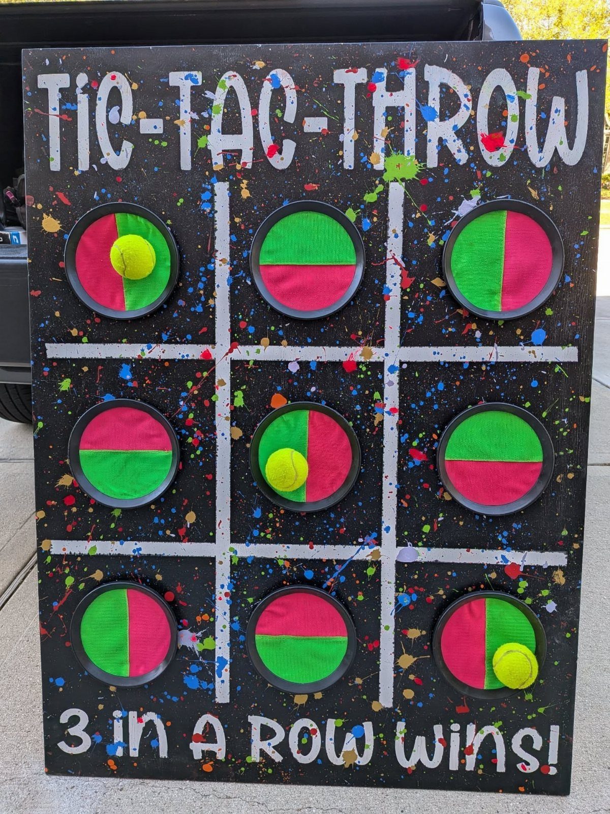 Tic-Tac-Throw carnival game board with colorful paint splatters and yellow balls