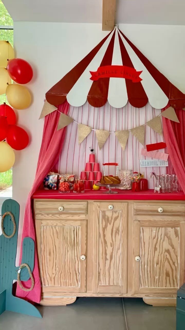Circus party setup with red and white striped tent backdrop and wooden sideboard.