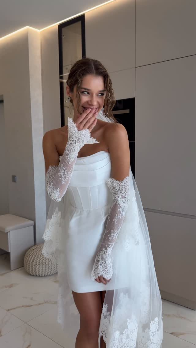 Woman in a short strapless white wedding dress with lace gloves and veil.