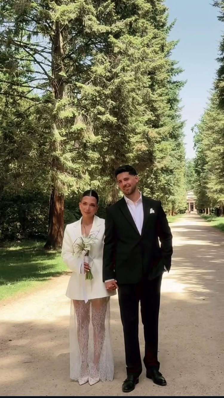 Couple on a tree-lined path, woman wearing a white blazer and sheer lace skirt.