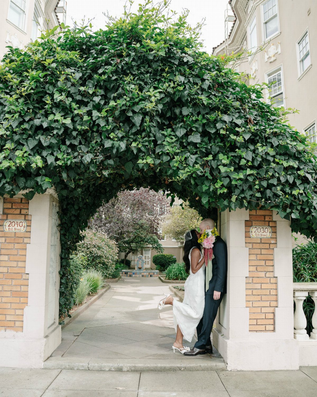 Couple embracing under an ivy arch, woman wearing a white satin slip dress.