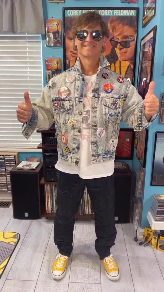 Man in 80s style denim jacket with pins, sunglasses, and yellow sneakers.