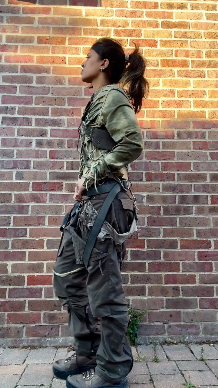Woman in distressed olive green tactical clothing and cargo pants against brick wall