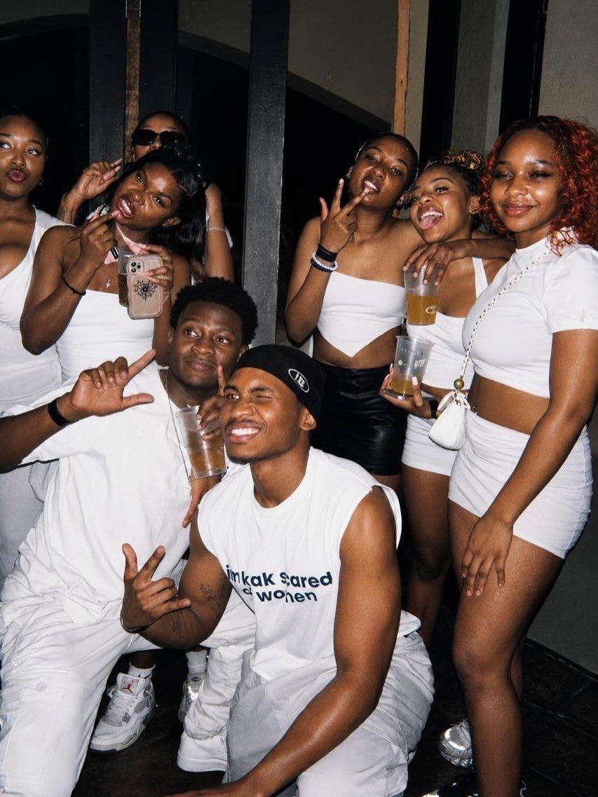 Group of young adults posing and smiling while wearing all-white party outfits.