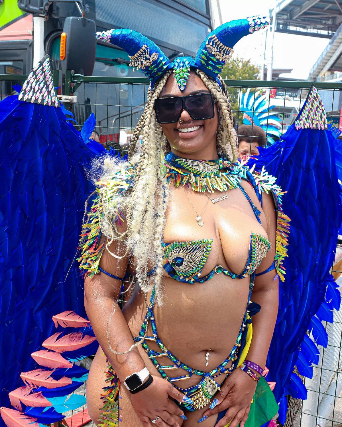 Woman in a blue feathered carnival costume with horned headpiece and sunglasses.