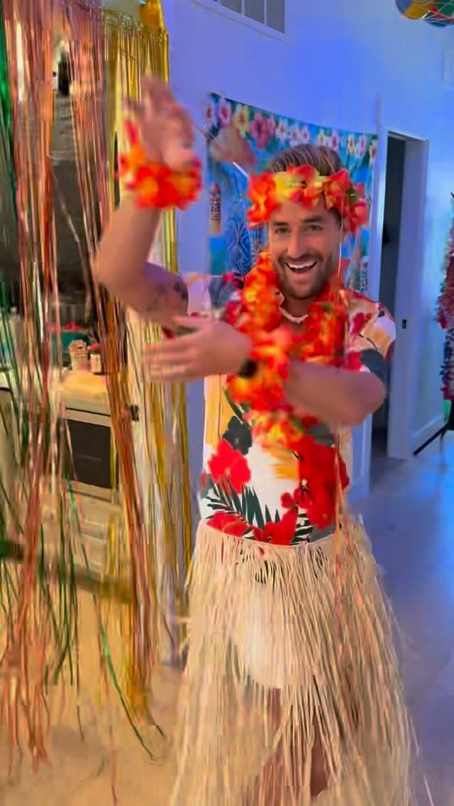 Man in a tropical party outfit with hula skirt and flower leis.