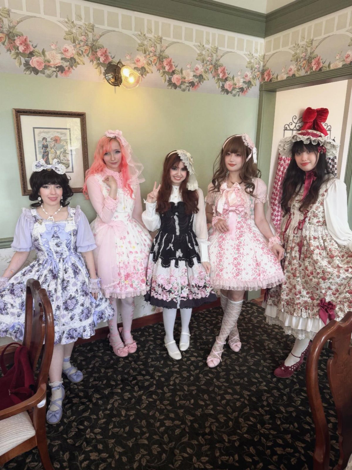 Five women wearing ornate Lolita fashion dresses posing in a decorated room.