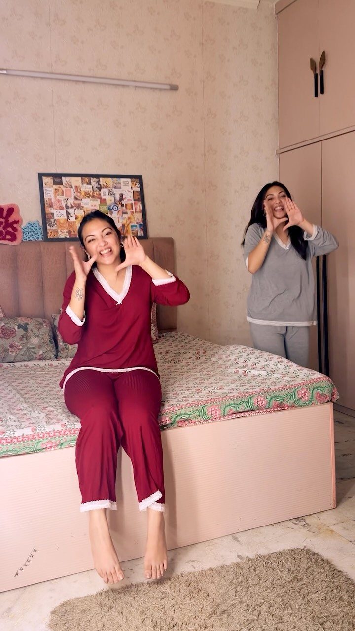 Two women wearing pajama sets posing in a bedroom on a bed.
