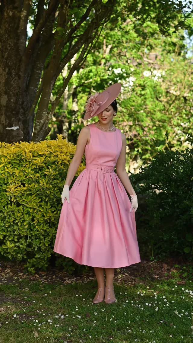 Woman in a vintage pink dress and hat posing in a lush green garden