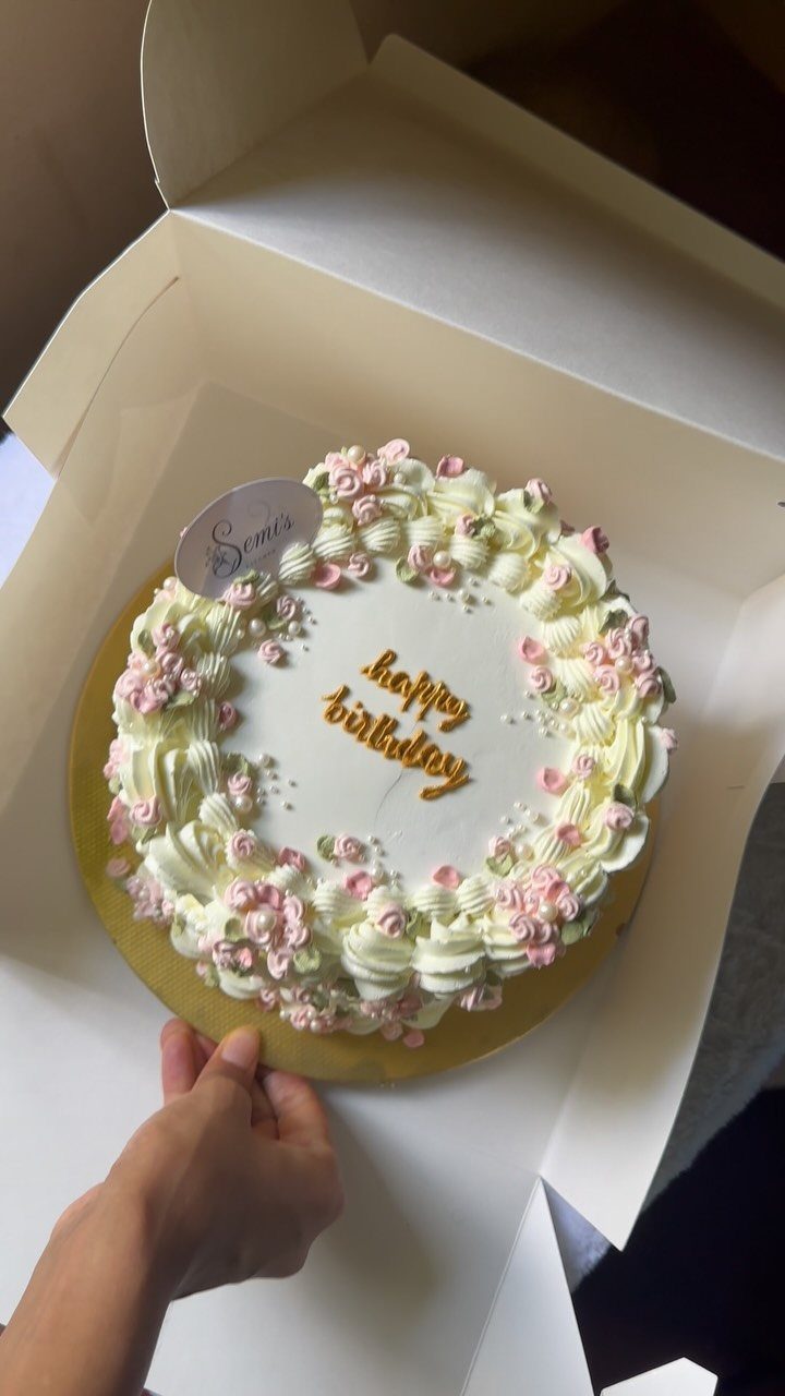 White birthday cake with buttercream swirls and pink flowers in a white box