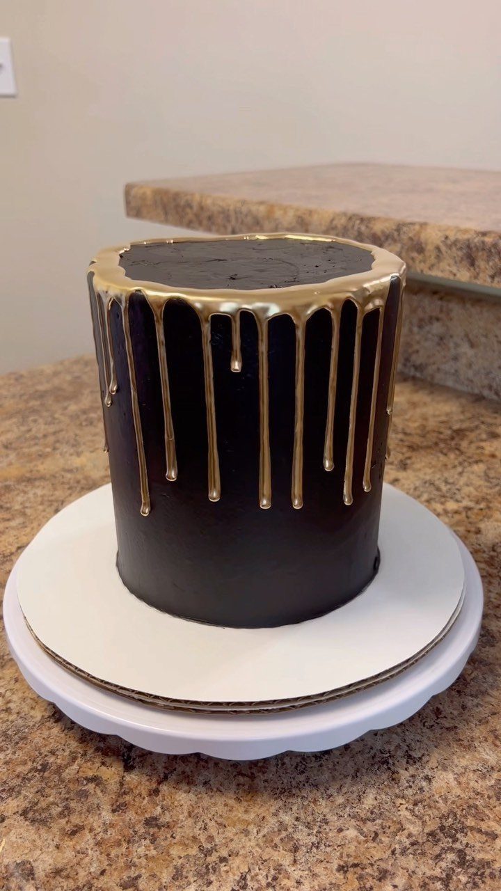 Black frosted cake with metallic gold glaze dripping down the sides on a stand