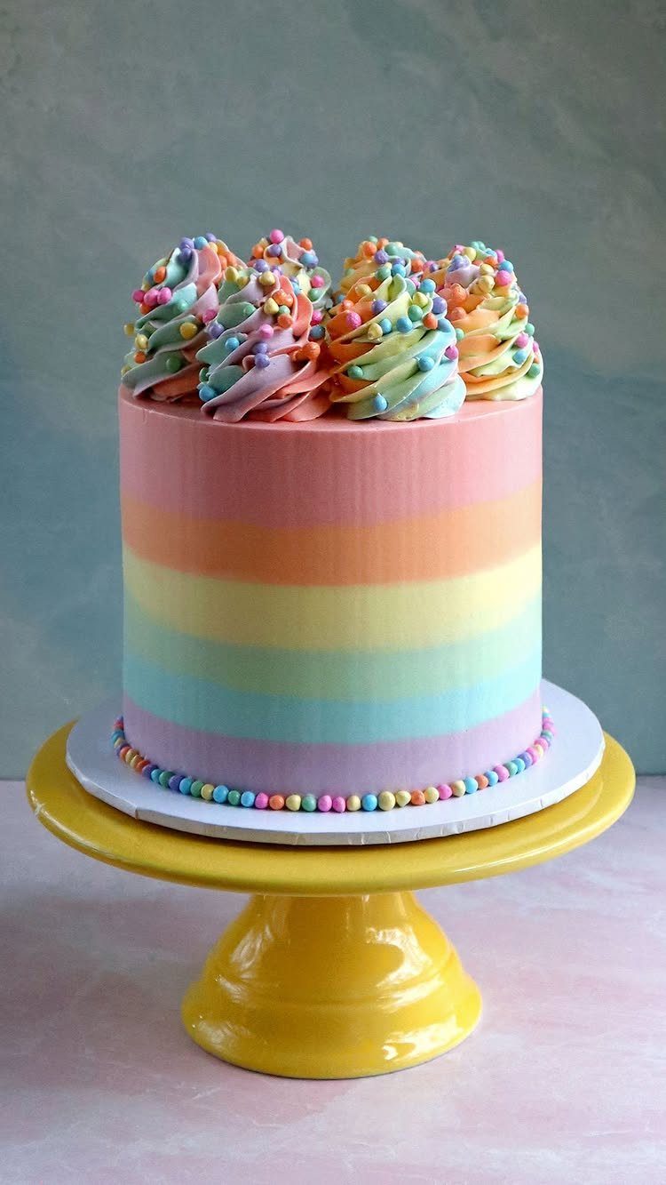 Rainbow striped cake with colorful buttercream swirls on a yellow cake stand