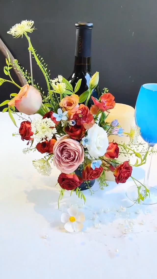 Floral arrangement of red and pink roses in a dark wine bottle centerpiece.