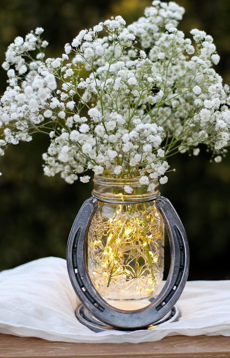 Mason jar with baby's breath and fairy lights encircled by a metal horseshoe.