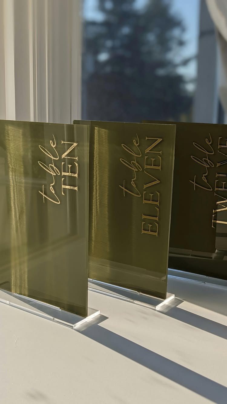 Olive green acrylic table number signs with gold lettering on clear stands.