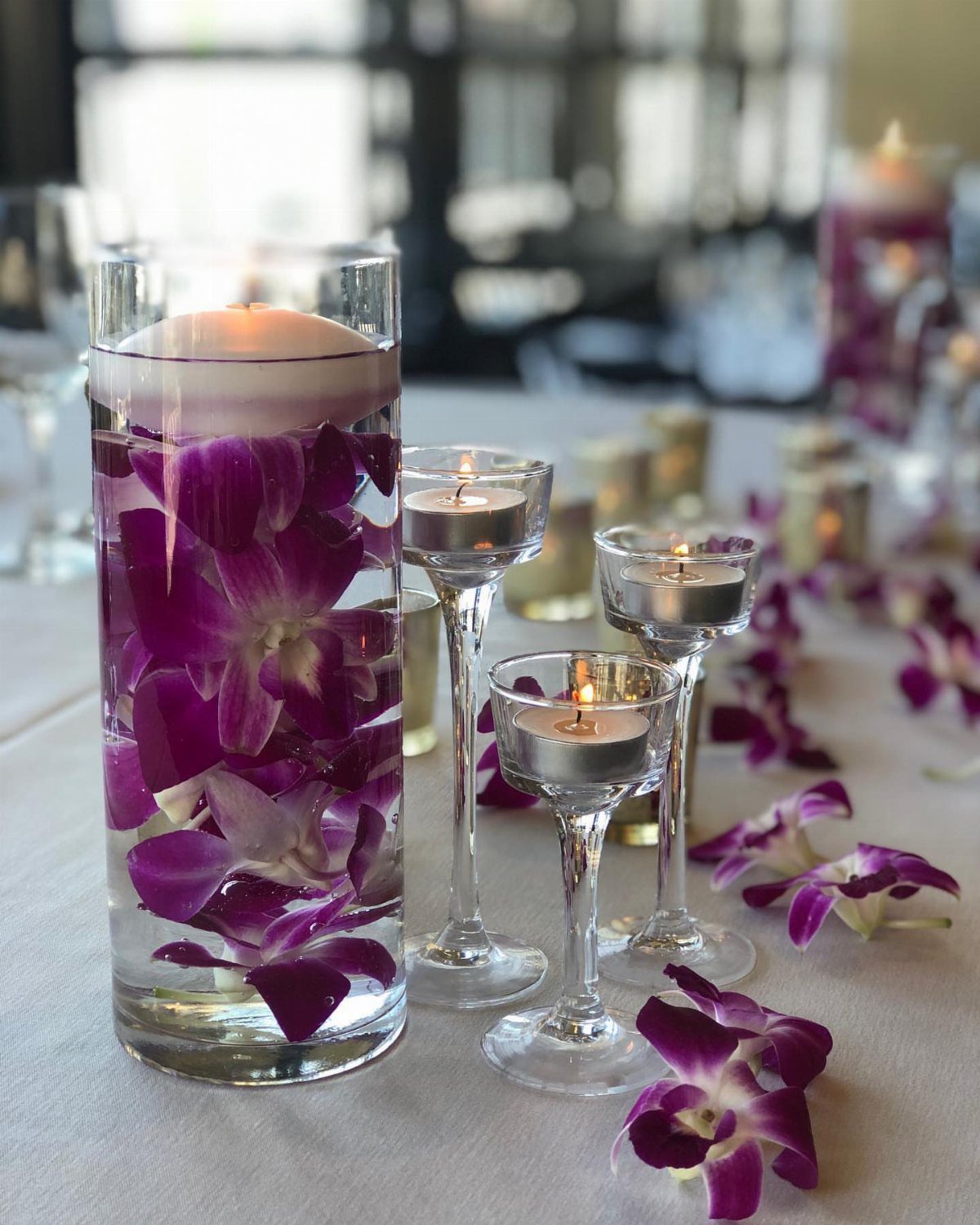 Tall glass cylinder with purple orchids and floating candle on white wedding table