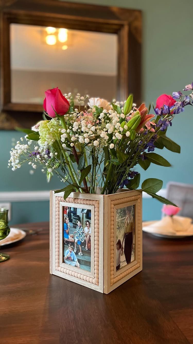 Square white photo frame centerpiece holding a colorful floral bouquet on a wooden table