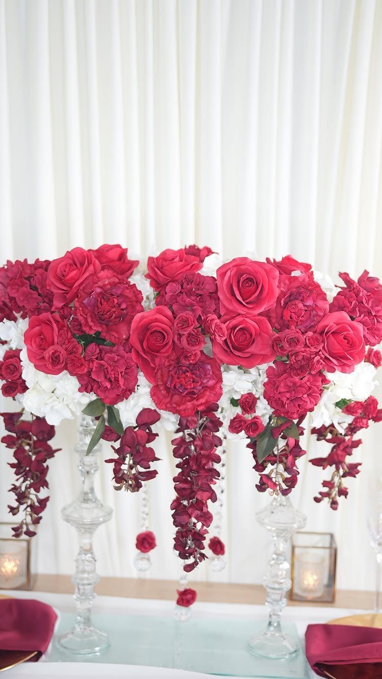 Red rose and carnation centerpiece on glass pedestals against white fabric backdrop