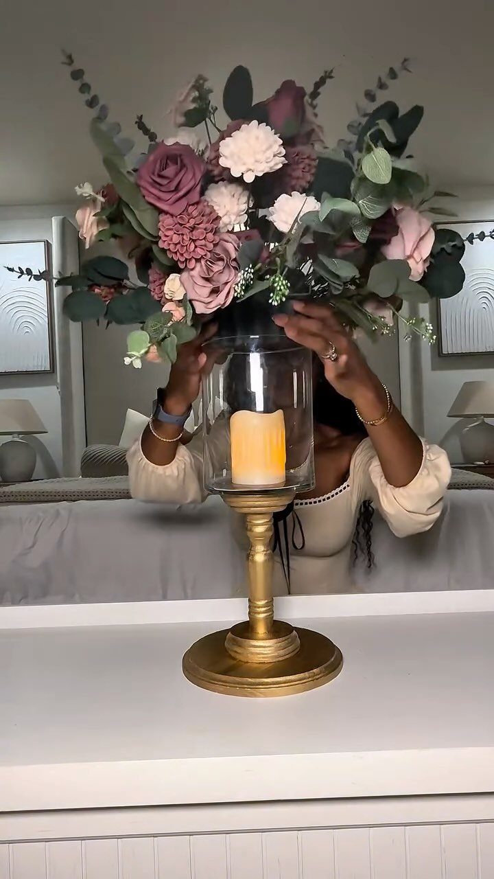 Gold pedestal candle holder topped with a lush pink and burgundy floral arrangement.