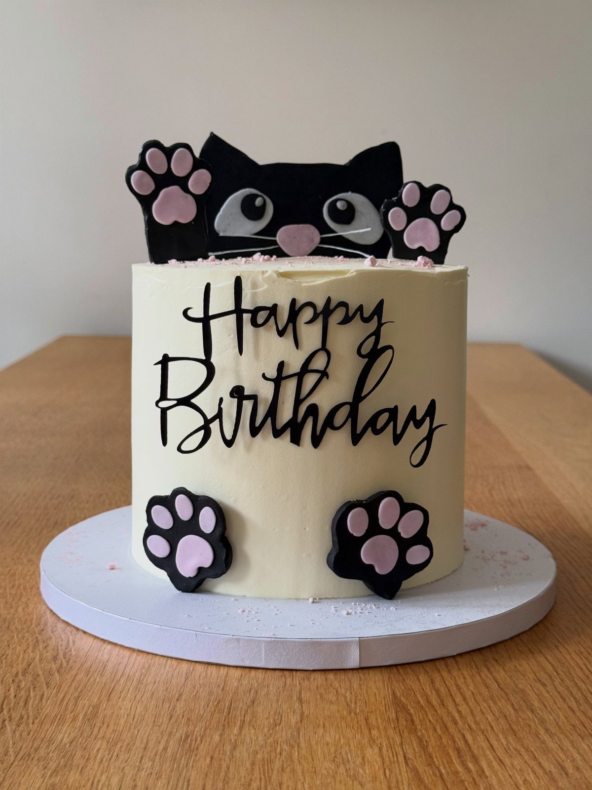 White birthday cake decorated with a black cat peeking over the top edge.