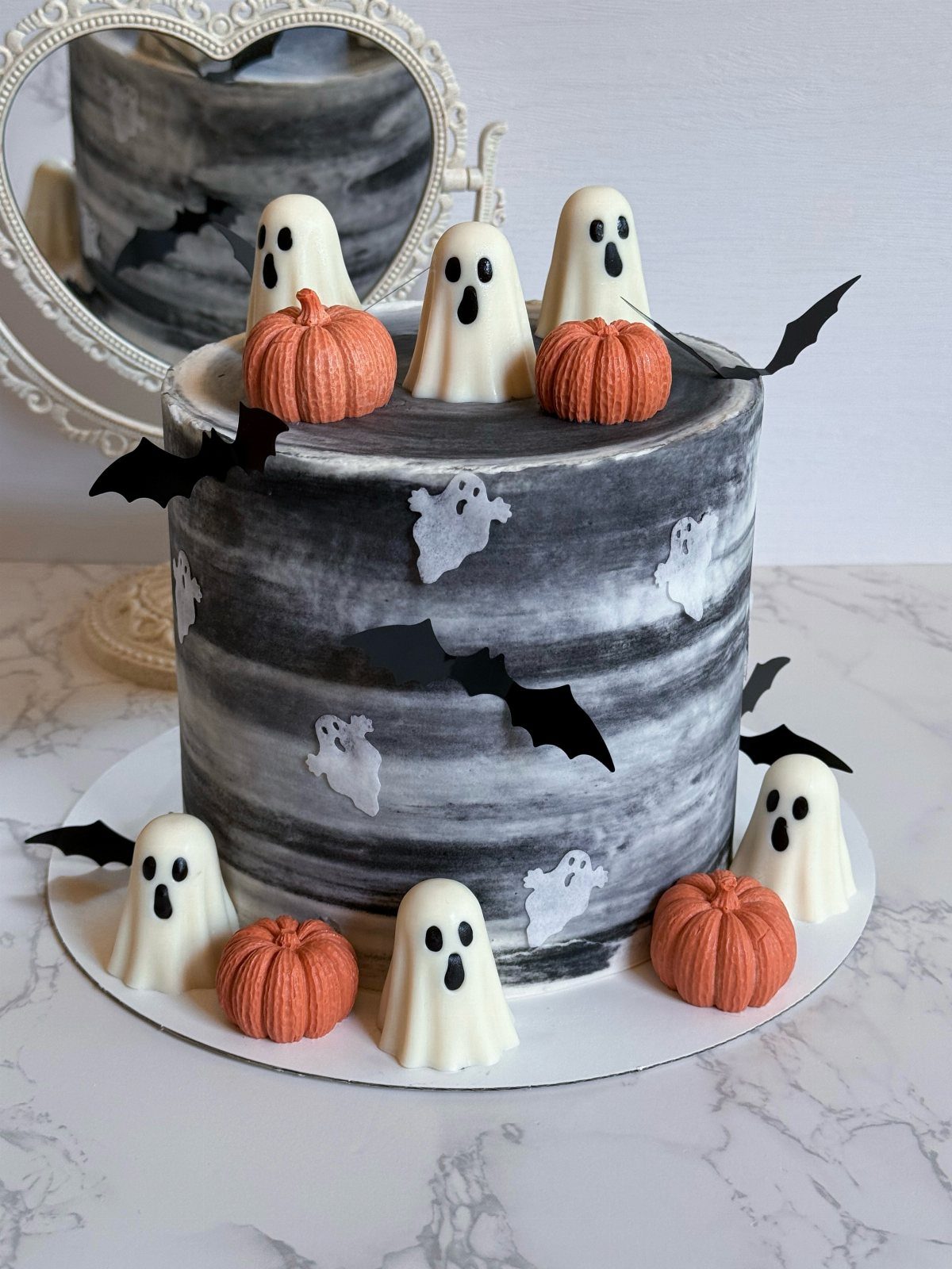 Marbled grey cake decorated with white ghost figures, orange pumpkins, and black bats.