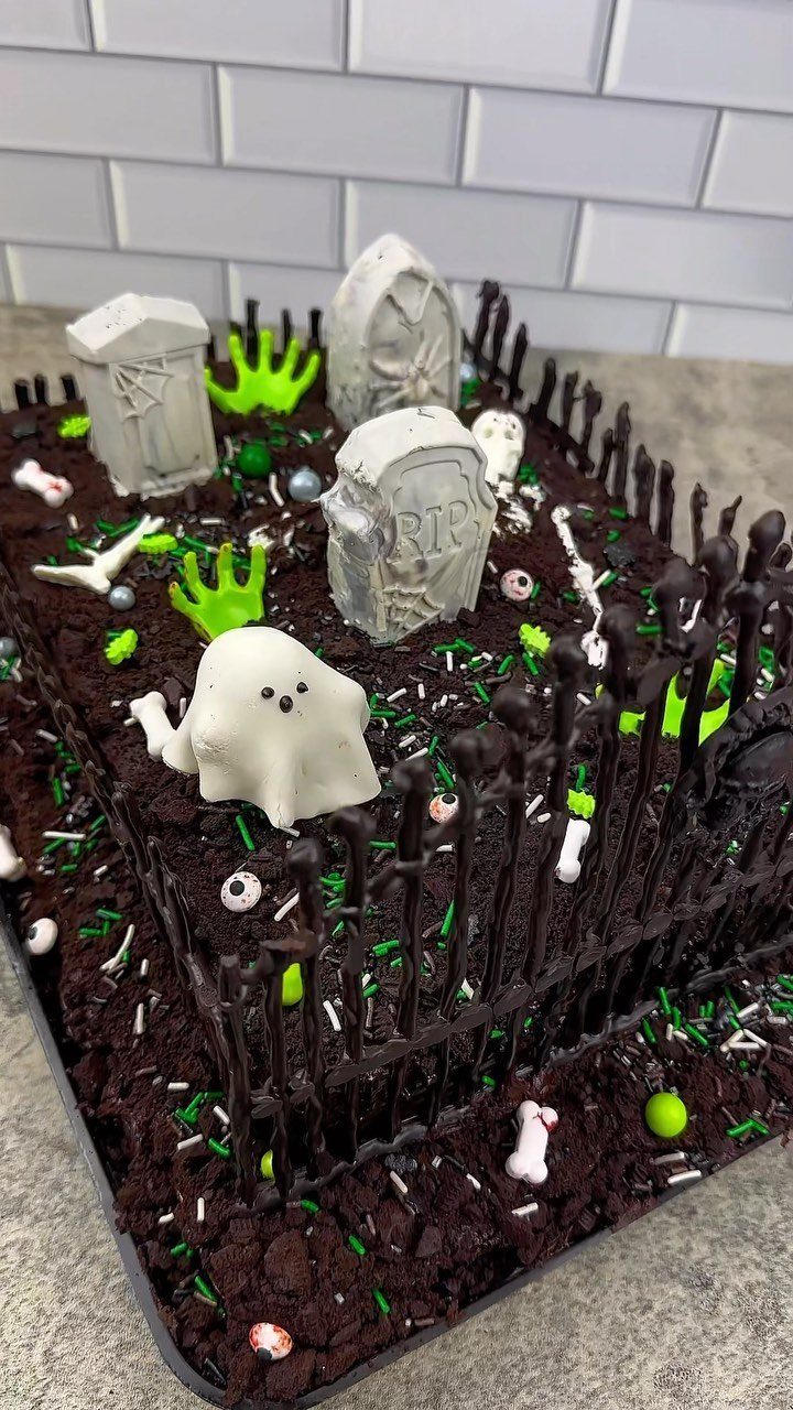 Graveyard cake with chocolate soil, grey tombstones, a white ghost, and chocolate fence.