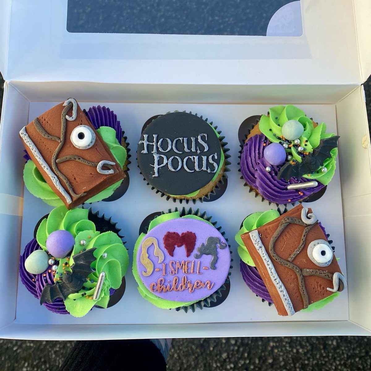 Hocus Pocus themed cupcakes with purple and green frosting in a white box