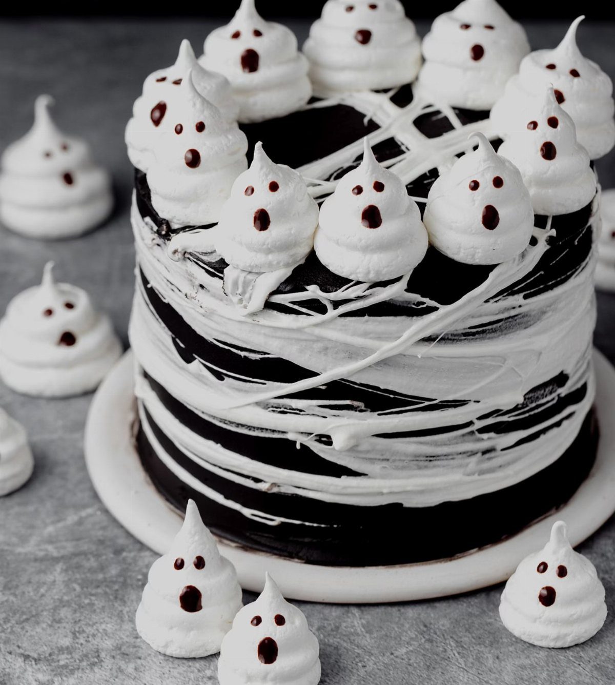 Chocolate cake decorated with small white meringue ghosts and white frosting swirls.