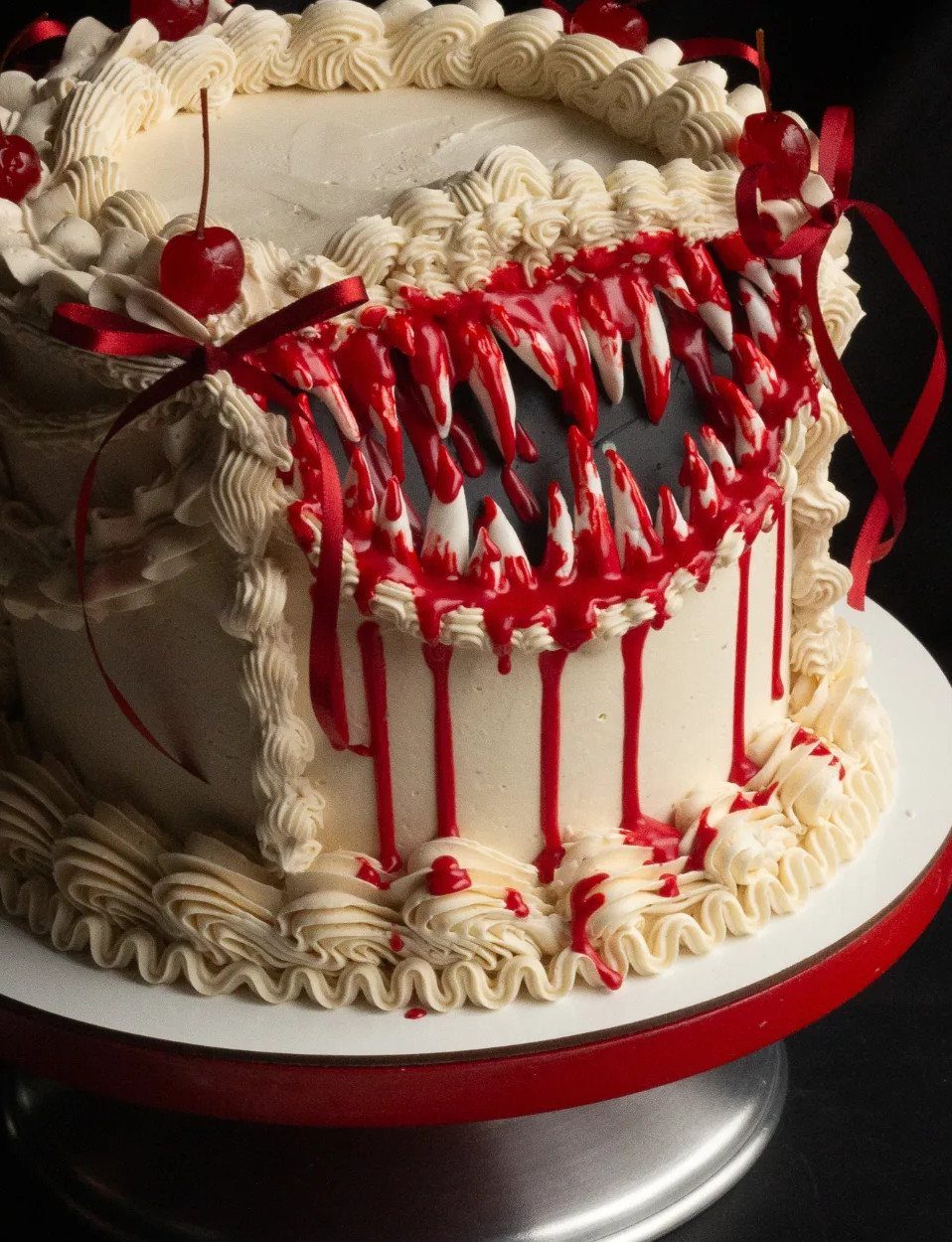 White frosted cake with a monster mouth, sharp teeth, and dripping red glaze.