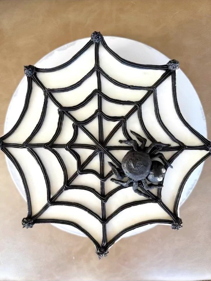 White frosted cake with a black icing spider web and a black spider.