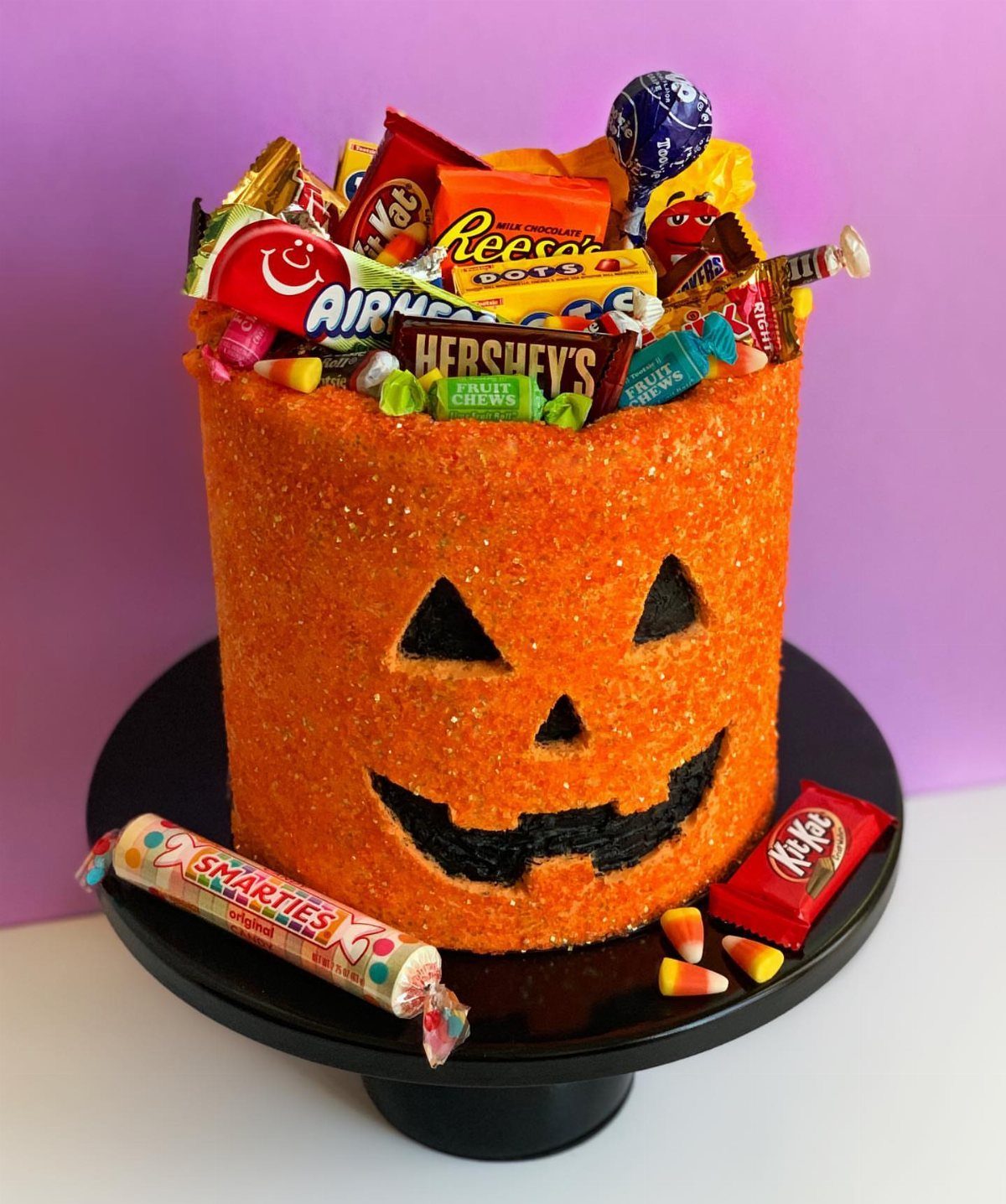 Jack-o'-lantern cake filled with assorted colorful candies on a black cake stand